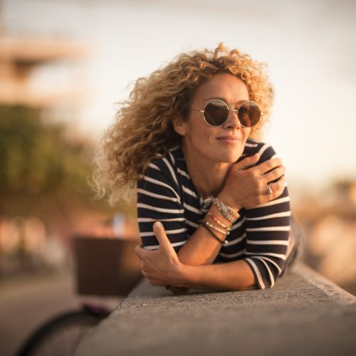 Relaxed and quiet happy beautiful curlly blonde adult caucasian woman lay down and ennjoy the sun inoutdoor leisure activity alone - people and summer sensations